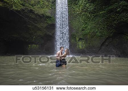 Stock Image - Young couple embracing in river by Tibumana Waterfall in Bali, Indonesia. Fotosearch