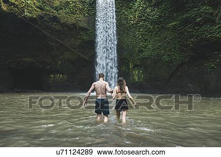 Stock Photo - Young couple holding hands in river by Tibumana Waterfall in Bali, Indonesia. Fotosearch