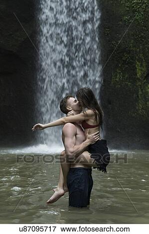 Stock Photo - Young couple kissing in river by Tibumana Waterfall in Bali, Indonesia. Fotosearch