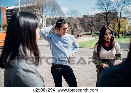 Picture - Young female and male adult friends chatting in city park. Fotosearch