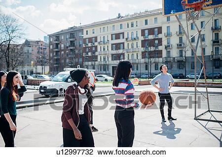 Stock Image - Young female and male adult friends playing basketball on city court. Fotosearch