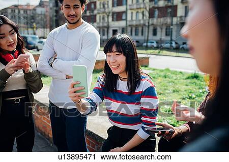 Stock Image - Young female and male adult friends using smartphones near city street. Fotosearch