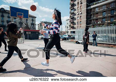 Stock Image - Young female and male adult friends playing basketball on city basketball court. Fotosearch