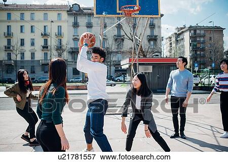 Stock Photo - Young female and male adult friends playing basketball on city court. Fotosearch