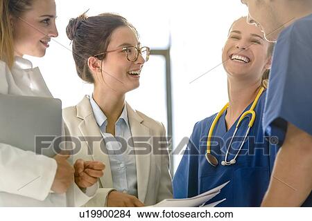Picture - Young female and male junior doctors chatting and laughing in hospital. Fotosearch