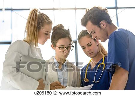 Stock Image - Young female and male junior doctors looking at medical records in hospital. Fotosearch