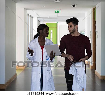 Picture - Young female and male scientists having discussion in laboratory corridor. Fotosearch