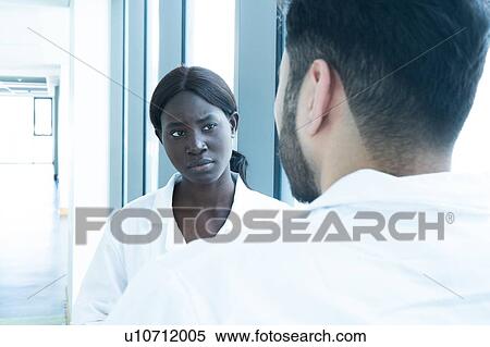 Stock Photography - Young female and male scientists having discussion in laboratory, over shoulder view. Fotosearch
