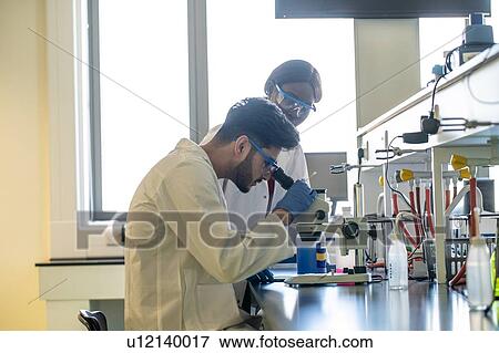 Young female and male scientists looking through microscope in laboratory View Large Photo Image Stock Photo - Young female and male scientists looking through microscope in laboratory. Fotosearch