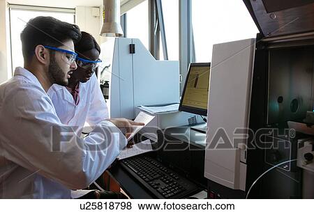 Stock Photo - Young female and male scientists reading paperwork in laboratory. Fotosearch
