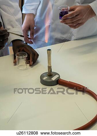 Stock Photo - Young female and male scientists experimenting with liquid and bunsen burner in laboratory, cropped. Fotosearch