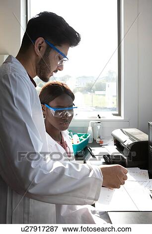 Young female and male scientists looking at paperwork in laboratory View Large Photo Image Stock Photo - Young female and male scientists looking at paperwork in laboratory. Fotosearch