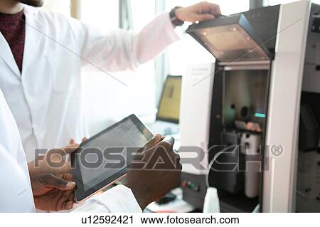 Stock Image - Young female and male scientists using digital tablet in laboratory, mid section. Fotosearch