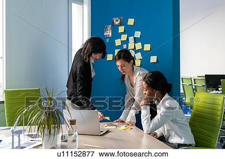 Stock Photo - Young female business creative team having sticky notes brainstorm meeting at desk in open plan office. Fotosearch