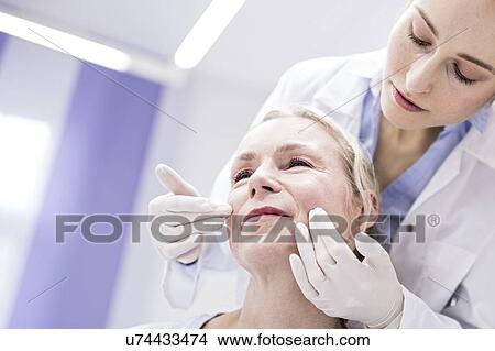 Picture - Young female doctor examining patient's face.. Fotosearch