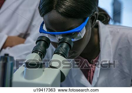 Stock Image - Young female scientist looking through microscope in laboratory, close up. Fotosearch