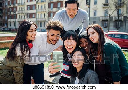Stock Image - Young male and female adult friends taking smartphone selfie near city street. Fotosearch