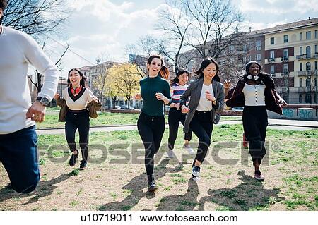 Stock Image - Young male and female adults running in park. Fotosearch