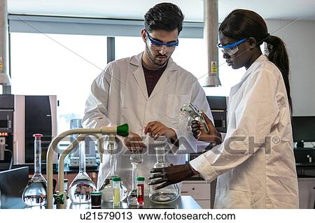 Stock Image - Young male and female scientists preparing experiment with sample bottles in laboratory. Fotosearch