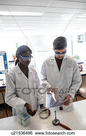 Stock Photograph - Young male and female scientists using pipette and bunsen burner in laboratory experiment. Fotosearch