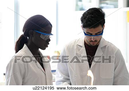 Stock Photography - Young male and female scientists using bunsen burner in laboratory experiment. Fotosearch