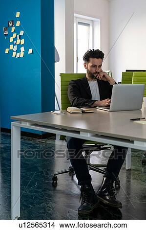Picture - Young male business creative looking at laptop in office. Fotosearch
