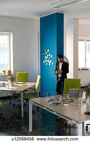 Young male business creative looking at smartphone in open plan office View Large Photo Image Stock Photo - Young male business creative looking at smartphone in open plan office. Fotosearch