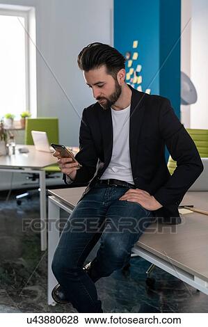 Young male business creative looking at smartphone in open plan office View Large Photo Image Stock Photo - Young male business creative looking at smartphone in open plan office. Fotosearch