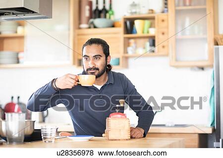 Young man at kitchen counter drinking fresh coffee View Large Photo Image Stock Photo - Young man at kitchen counter drinking fresh coffee. Fotosearch