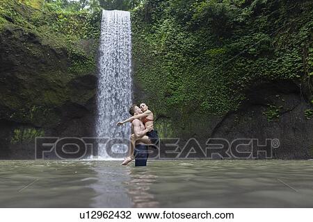 Young man carrying young woman in river by Tibumana Waterfall in Bali, Indonesia View Large Photo Image Stock Image - Young man carrying young woman in river by Tibumana Waterfall in Bali, Indonesia. Fotosearch