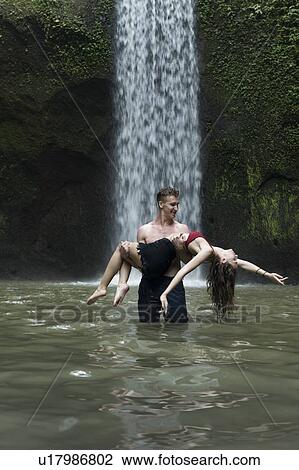 Young man carrying young woman in river by Tibumana Waterfall in Bali, Indonesia View Large Photo Image Stock Image - Young man carrying young woman in river by Tibumana Waterfall in Bali, Indonesia. Fotosearch