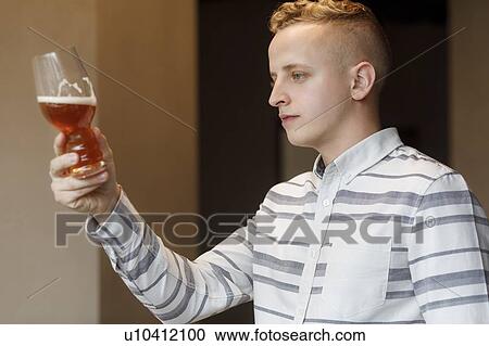 Stock Image - Young man examining glass of beer. Fotosearch