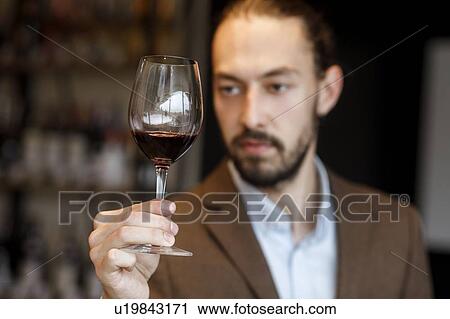 Stock Image - Young man examining glass of wine. Fotosearch