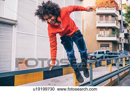 Stock Image - Young man jumping over divider on pavement, Milano, Lombardia, Italy. Fotosearch