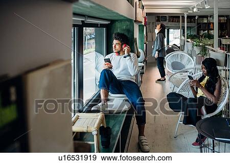 Stock Photo - Young man listening to headphones in cafe window seat. Fotosearch