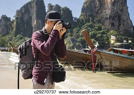 Stock Photo - Young man photographing on beach in Krabi, Thailand. Fotosearch