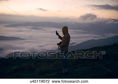 Stock Image - Young man photographing with smart phone at sunset in the Carpathian Mountain Range. Fotosearch