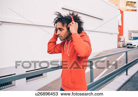 Young man putting on headphones walking past concrete wall View Large Photo Image Stock Image - Young man putting on headphones walking past concrete wall. Fotosearch