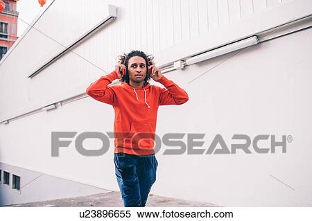 Young man putting on headphones walking past concrete wall View Large Photo Image Stock Photography - Young man putting on headphones walking past concrete wall. Fotosearch
