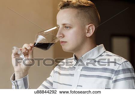 Stock Image - Young man smelling wine in glass at tasting. Fotosearch