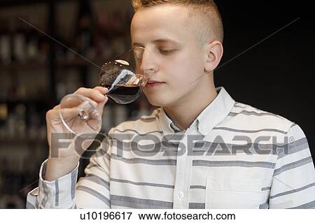 Stock Photo - Young man smelling wine in glass at tasting. Fotosearch