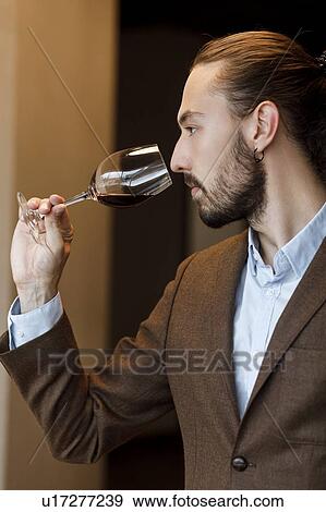 Stock Photo - Young man smelling wine in glass at tasting. Fotosearch