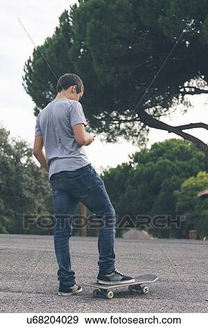 Young man texting while standing on skateboard View Large Photo Image Stock Photo - Young man texting while standing on skateboard. Fotosearch