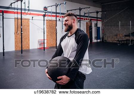 Stock Image - Young man training, lifting atlas ball in gym. Fotosearch
