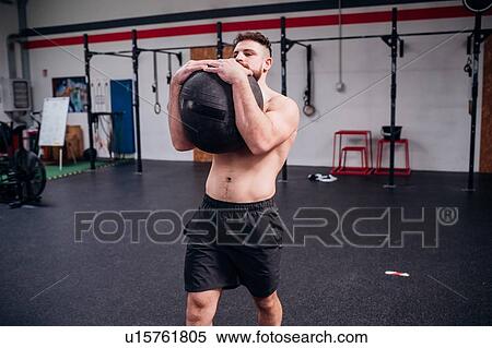Young man training, lifting atlas ball in gym View Large Photo Image Stock Photography - Young man training, lifting atlas ball in gym. Fotosearch
