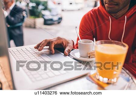 Stock Photograph - Young man using laptop at cafe. Fotosearch