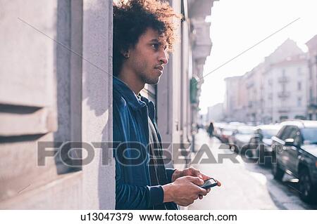 Young man using smartphone on pavement, Milano, Lombardia, Italy View Large Photo Image Stock Photo - Young man using smartphone on pavement, Milano, Lombardia, Italy. Fotosearch