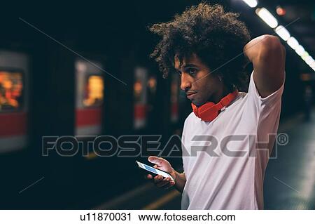Stock Image - Young man using smartphone on train platform. Fotosearch