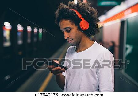 Stock Photograph - Young man using smartphone on train platform. Fotosearch