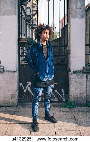 Stock Image - Young man waiting in front of gate, Milano, Lombardia, Italy. Fotosearch